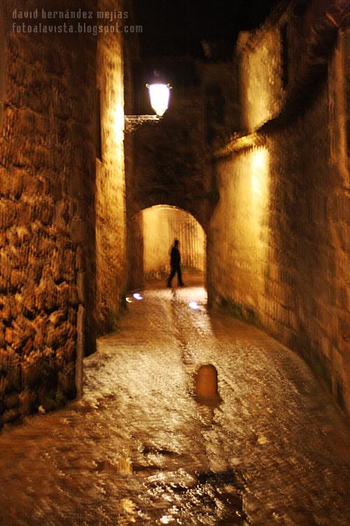 Silueta humana caminante bajo un arco vista callejeando bajo la lluvia entre los muros del centro histórico de Baeza, Jaén