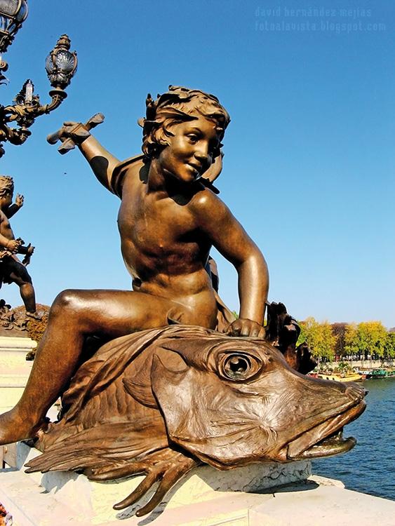 Fotografía de conjunto escultórico de un niño, que bien podría ser un amorcillo, subido a lomos de un enorme pez sobre el puente de Alejandro III, de París (Francia)