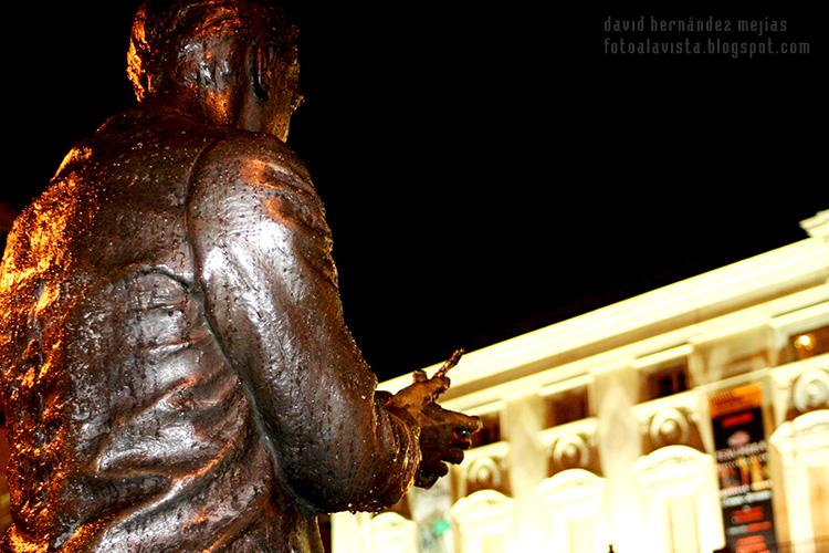 Detalle de la escultura en bronce con gotas de lluvia de Federico García Lorca soltando una paloma en la noche en frente del Teatro Español, Madrid