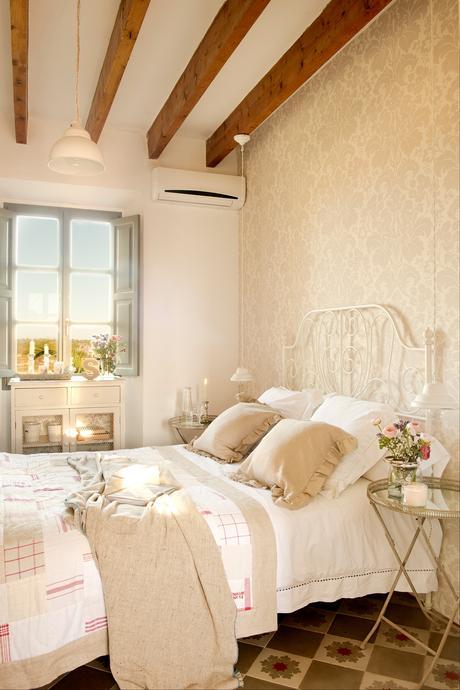 Dormitorio en beige con pared con papel pintado, cama de forja blanca, mosaico hidráulico, veladores como mesillas y mueble bajo ventana 00378454 O