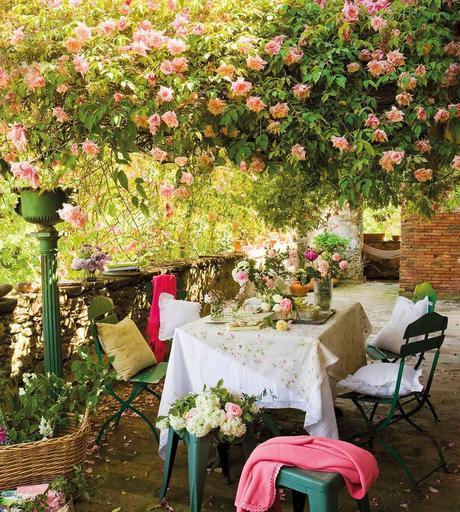 Comedor de exterior con sillas de hierro verde bajo pérgola cubierta de rosas_00365587b