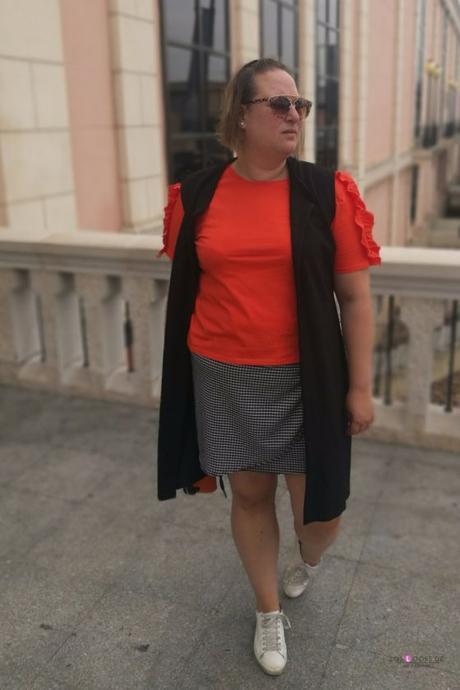look talla grande curvy con camiseta naranja con volantes en las mangas de primark con falda cuadros vichy y sneakers zapatillas de deporte blancas y maxi chaleco negro de asos para un outfit de verano