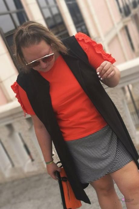 look talla grande curvy con camiseta naranja con volantes en las mangas de primark con falda cuadros vichy y sneakers zapatillas de deporte blancas y maxi chaleco negro de asos para un outfit de verano