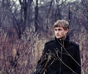 Un hombre de negro camina entre los arbustos que crecen bajo el bosque