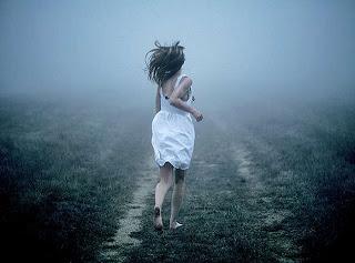 Mujer con vestido blanco y descalza huyendo por un campo hacia la niebla.