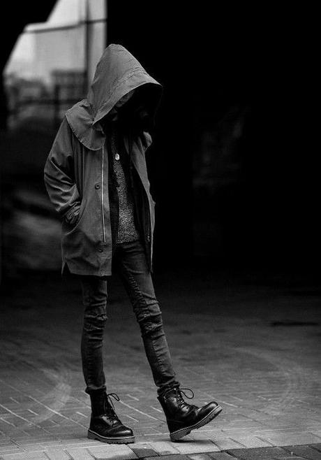 Muchacha joven paseando bajo la lluvia. Lleva una capucha que le tapa la cara, ropa vaquera y botas tipo militar negras.