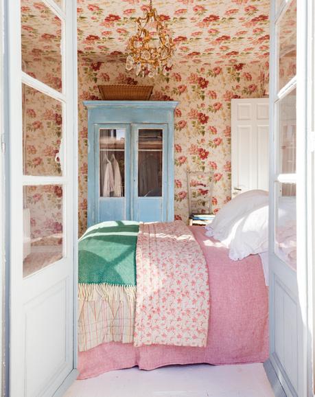Dormitorio con paredes y techo con papel pintado de flores, vitrina azul y ropa de cama rosa_457375
