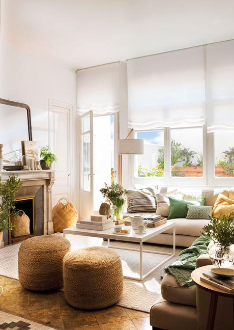 Salón con chimenea y mesa de centro cuadrada encima de alfombra con sofás blancos y pufs de fibras naturales