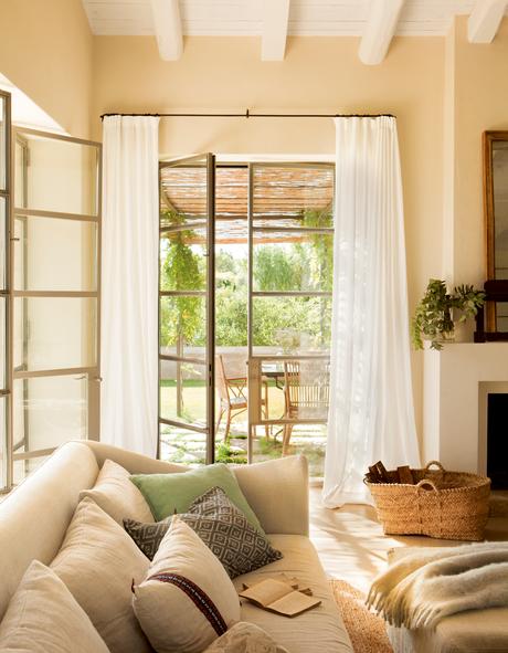 Salón en tonos verdes con amplia ventana con visillos, sofá, chimenea y cesta de fibra_402344