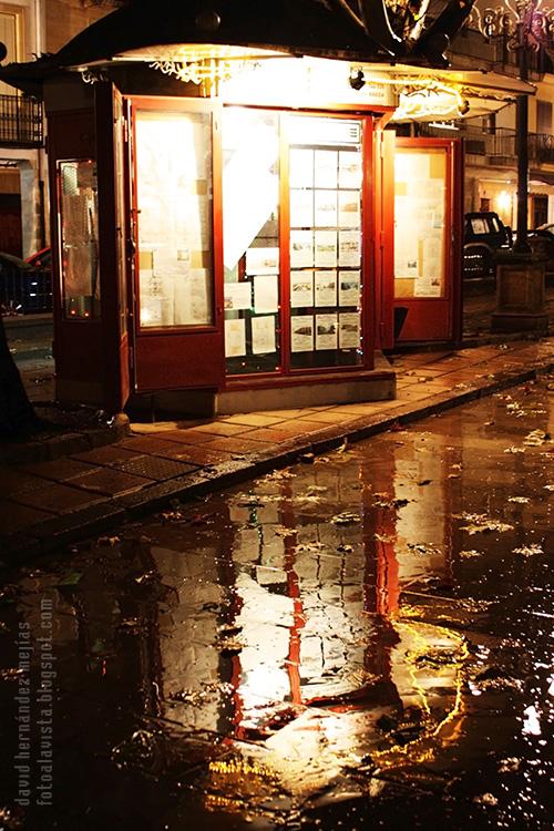 Fotografía de un quiosco-inmobiliaria produciendo fantásticos reflejos en una noche lluviosa de Baeza, Jaén