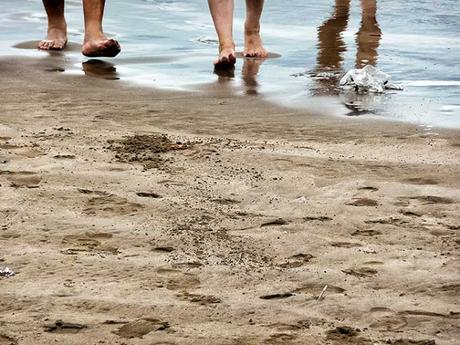 Un par de pies saliendo del agua y la arena que los espera.
