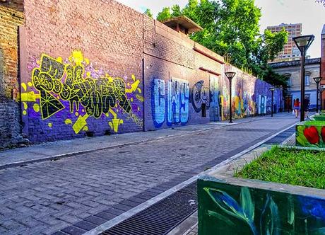 Callle empedrada interna de plaza bordeado ppor un murallon pin tado con grafittis.