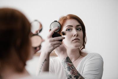 Mujer poniéndose polvos con una brocha delante de un espejo