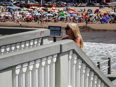 La chica en la escalera. Joven en escalera y de fondo la gente en la playa.
