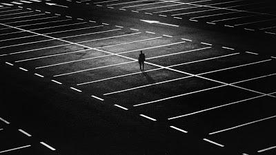 imagen que muestra aparcamiento vacío de noche, con una persona sola vista de lejos. soledad y abandono