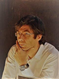Fotografía del escritor Ruy Vega, que aparece con el pelo semi largo, gafas sin montura, sin barba, camisa blanca y la mano puesta en la cara en actitud pensante.