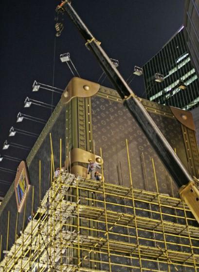 Workers dismantle a giant advertisement display modeling a Louis Vuitton suitcase outside a Louis Vuitton branch on Thursday, May 19,