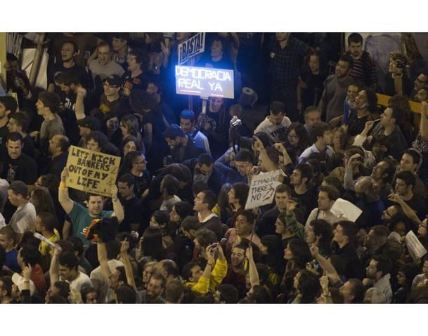 Demonstrators hold placards as other demonstrators gather in Madrid's Puerta del Sol