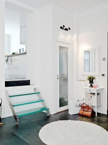 suelo de losas de piedra italiana sofá chaiselong salón y cocina en dos niveles piso sueco piso en dos niveles paredes redondeadas muebles de cocina bajos estilo nórdico estilo escandinavo escaleras de cristal diseño de interiores decoración sueca decoración de interiores cuadro con zapatos colcha rosa cocina moderna cocina blanca 