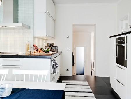 suelo de losas de piedra italiana sofá chaiselong salón y cocina en dos niveles piso sueco piso en dos niveles paredes redondeadas muebles de cocina bajos estilo nórdico estilo escandinavo escaleras de cristal diseño de interiores decoración sueca decoración de interiores cuadro con zapatos colcha rosa cocina moderna cocina blanca 