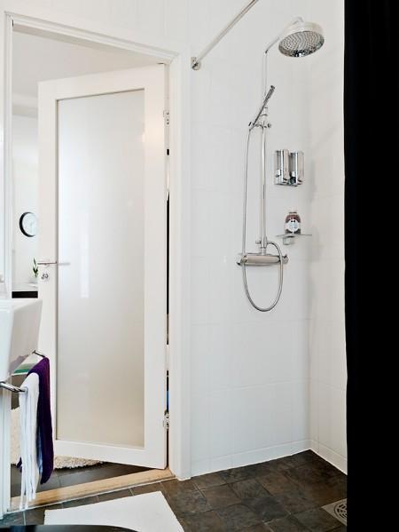 suelo de losas de piedra italiana sofá chaiselong salón y cocina en dos niveles piso sueco piso en dos niveles paredes redondeadas muebles de cocina bajos estilo nórdico estilo escandinavo escaleras de cristal diseño de interiores decoración sueca decoración de interiores cuadro con zapatos colcha rosa cocina moderna cocina blanca 