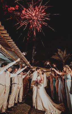 Novios con los invitados rodeándoles con bentagalas y fuegos artificiales de fondo