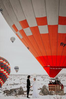 Novios con globos aerostáticos de fondo e invitados esperándoles en una barquilla