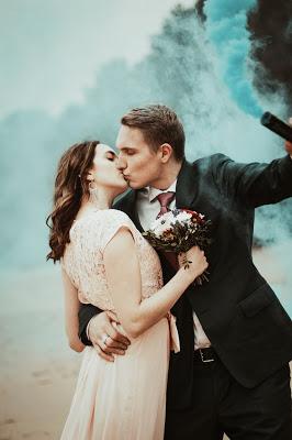 Pareja de novios posando mientras se besan con una antorcha de humo de color azul