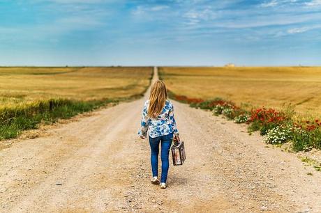 Mujer caminando con una maleta por una calle de lastre.