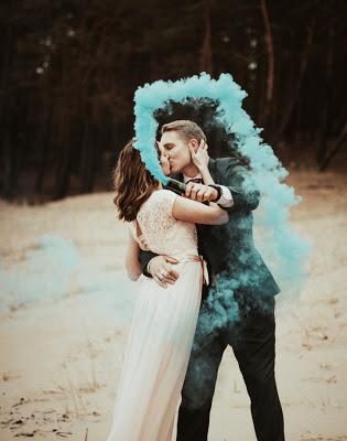 Novios en la playa lanzando una bomba de humo de color azul