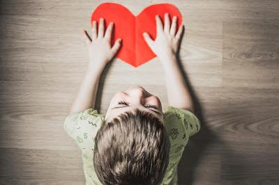 Niño con un corazón recortado en un papel rojo