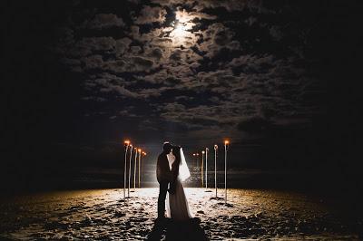 Novios en una playa de noche cerrada iluminados por la luna y antorchas