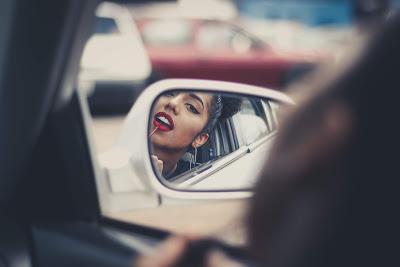 Chica maquillándose los labios en el coche mirándose en el retrovisor