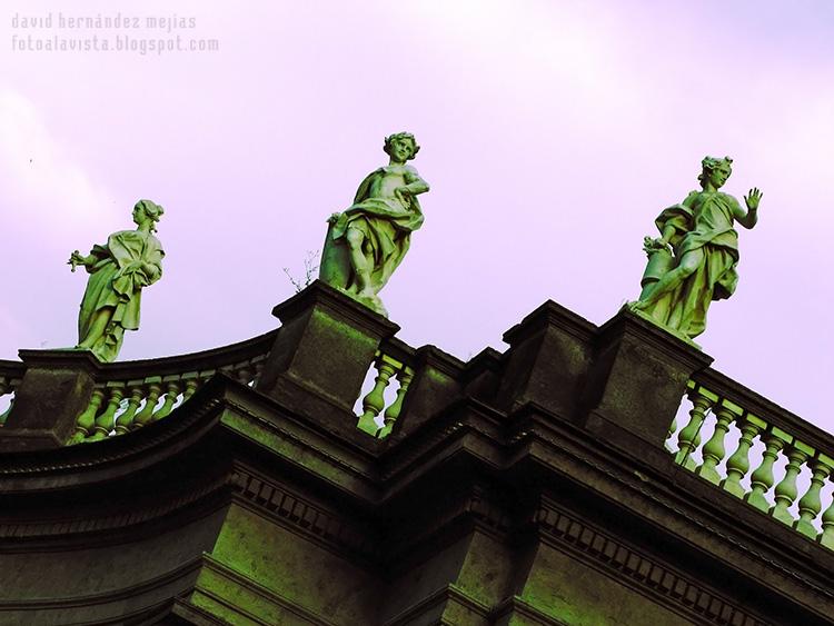 Contrapicado hacia el cielo con balaustrada y 3 esculturas en un edificio de Nápoles, Italia