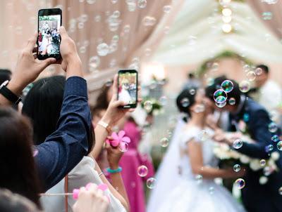 Novios besándose en una nube de burbujas e invitados con los móviles en alto fotografiando el momento 