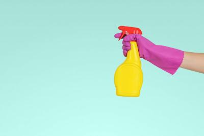 Mano con un guante sujetando una botella de espray limpiador Mano con un guante sujetando una botella de espray limpiador