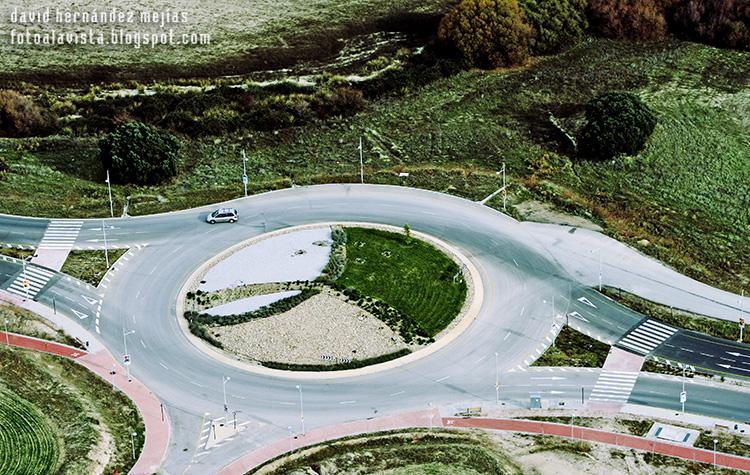 Fotografía tomada desde ultraligero volando por encima de una rotonda y carretera que cruza tierras de labranza a los lados en Villanueva del Pardillo, Madrid