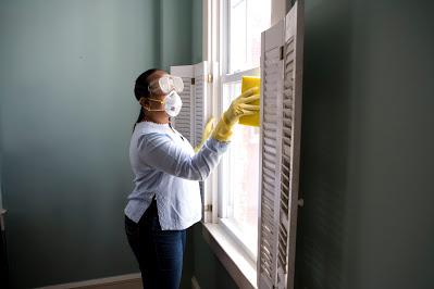 Mujer limpiando una ventana con mascarilla y gafas Mujer limpiando una ventana con mascarilla y gafas