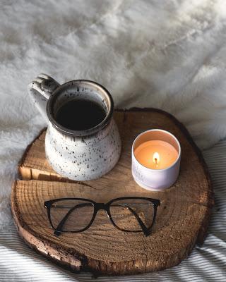 Vela en un contenedor junto a un café y unas gafas Vela en un contenedor junto a un café y unas gafas
