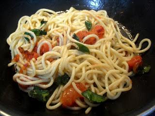 Salteando los espaguetis con el tomate, ajo y albahaca.