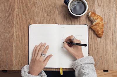 Mujer escribiendo en una agenda mientras desayuna
