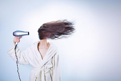 Mujer en albornoz secándose el pelo con un secador de forma intensa
