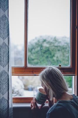 Mujer tomando café delante de una ventana a un paisaje invernal