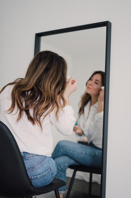 Mujer aplicándose un cosméticos sentada delante de un espejo