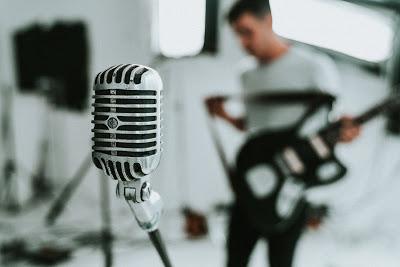 Micrófono y músico con su guitarra en segundo plano