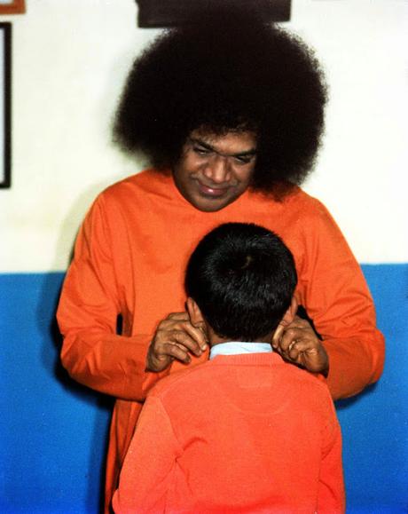 Sri Sathya Sai tirando de las mejillas a un niño