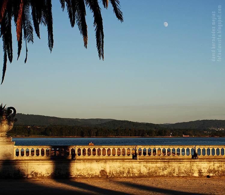 Paseo con balaustrada al mar, palmera y luna al atardecer en la isla de La Toja, Pontevedra, Galicia