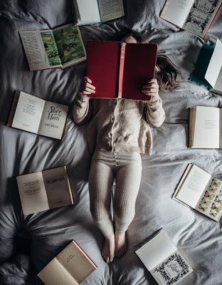 Mujer rodeada de libros abiertos leyendo en la cama Mujer rodeada de libros abiertos leyendo en la cama