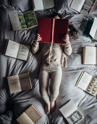 Mujer rodeada de libros abiertos leyendo en la cama