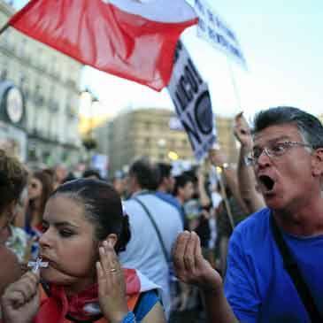 Un manifestante contra el gasto público en la visita del Papa a España chilla contra una peregrina que reza en la Puerta del Sol